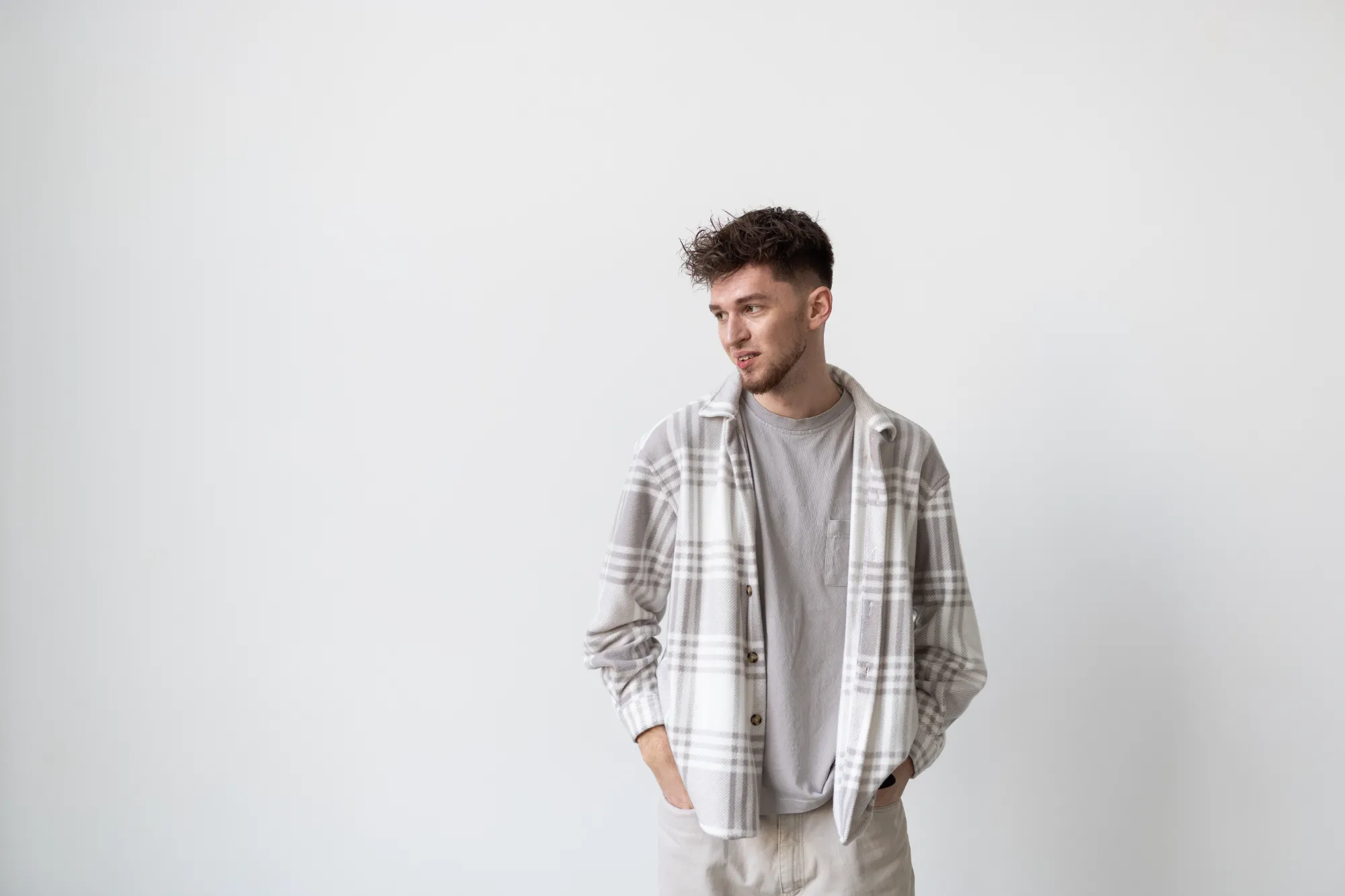young-man-holding-hands-pockets-looking-camera-while-standing-against-white-background